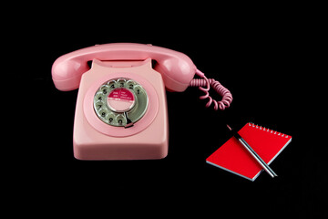 Vintage Pink Telephone with Pen and Notebook on a Black Background