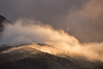 日光があたる雲と霧が広がる山の抽象的イメージ