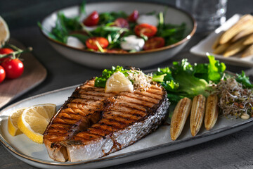 Close-up grilled salmon steak with mini corn, microgreen, salad and lemon. Fried salmon steak and...