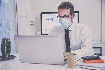 Business man with surgical masks working in the office during lockdown for coronavirus covid-19. Male sitting at the desk works with laptop at home. Health care, quarantine, remote working concept.