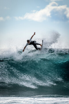 Young surfer with with wetsuit enjoying big waves in Tenerife, Canary Islands. Sporty boy riding his surf board on the ocean wave. Brave teenager making tricks on the rough sea during a competition.
