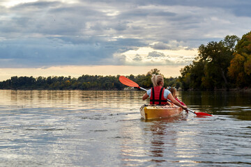 A mother kayaking with her young daughter on the river on a beautiful sunset along the coast with green trees and cloudy sky