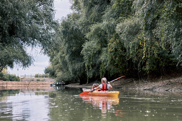 A mother kayaking with her young daughter on the river near coast with green willow trees