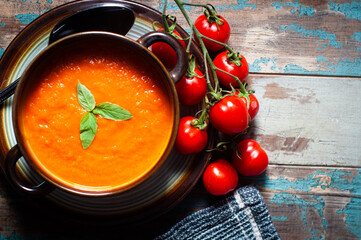Home made tomato soup served on a rustic wooden table and garnished with basil and vine ripened tomatoes.