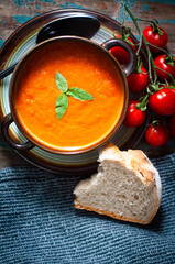 Home made tomato soup served on a rustic wooden table with freshly baked artisan bread and garnished with basil and vine ripened tomatoes.