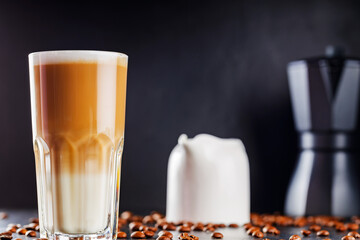 Latte macchiato coffee and scattered coffee beans. Latte macchiato and milk jug on a dark background. Italian hot drink
