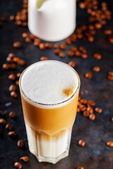 Latte macchiato coffee and scattered coffee beans. Latte macchiato and milk jug on a dark background. Italian hot drink