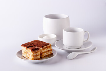 coffee cup, a slice of tiramisu lies on a white plate on a white background