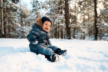 Fototapeta na wymiar A little boy in the snow. Happy child walking through winter forest