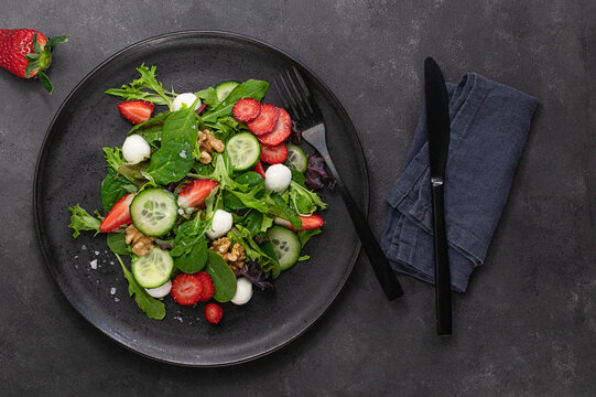 Table with a strawberry salad next to some cutlery