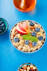 Oatmeal porridge and ingredients on a blue background. Oatmeal cereal, blueberries, nuts, apple slices and honey. Healthy vegetarian food concept. Top view
