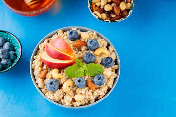 Oatmeal porridge and ingredients on a blue background. Oatmeal cereal, blueberries, nuts, apple slices and honey. Healthy vegetarian food concept. Top view