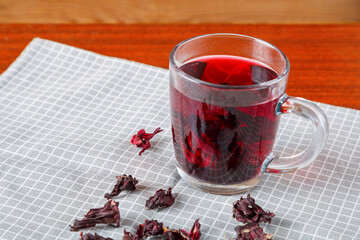 A cup of hibiscus tea and hibiscus petals on a white background.
