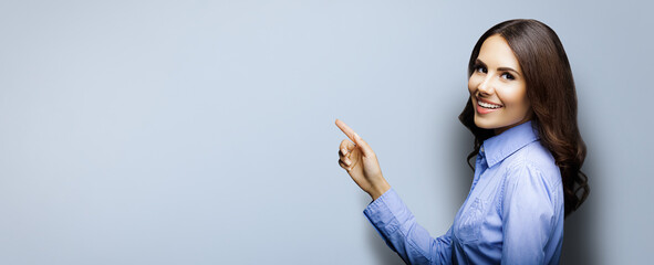 Portrait of smiling young businesswoman. Brunette girl pointing showing by index finger copy space...