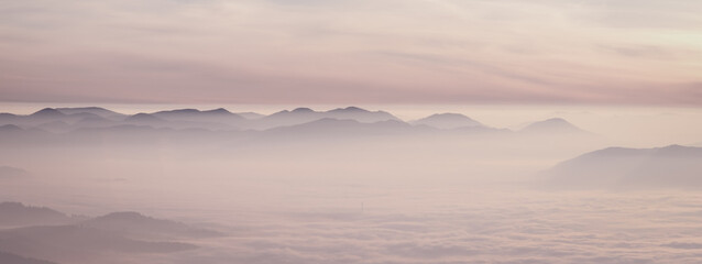 Mountain range with visible silhouettes through the morning colorful fog.