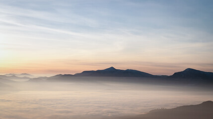 Mountain range with visible silhouettes through the morning colorful fog.