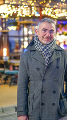 Fototapeta na wymiar Hombre de mediana edad con abrigo y bufanda con boké de fondo de luces amarillos