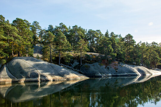 Sunny rocks that are reflected in the water. Pine forest on autumnal archipelago island.