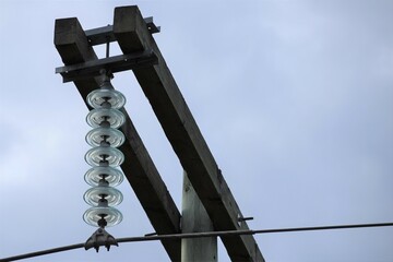 Power line with glass insulators and wires.  Room for copy.  Pale blue sky in background.