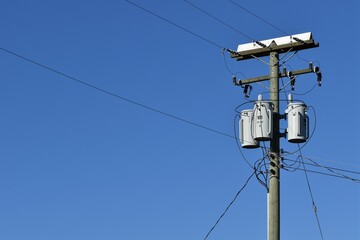 Power transformer on pole with power lines. Blue sky in background.