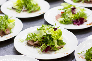 Many white plates with green salad
