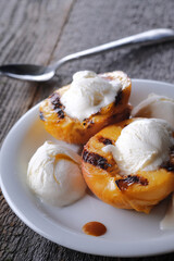 Sweet dessert consisting of vanilla ice cream balls and grilled peach halves and caramel sauce. Wooden grey background.