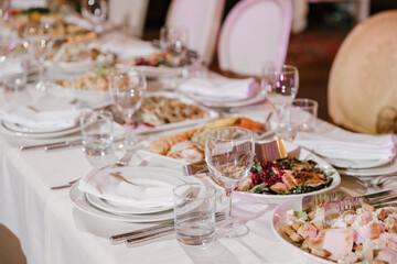 Table setting for a banquet or celebration.Empty glasses for alcoholic beverages, wine and juice, a set table.Cloth napkins on a white platter and cutlery on the table.Cold appetizers and salads