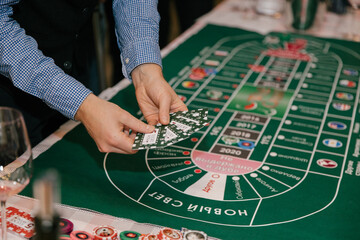 Close-up, hands of people playing in a wine casino, a man's hand with game chips on a green...