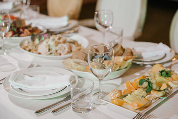 Table setting for a banquet or celebration.Empty glasses for alcoholic beverages, wine and juice, a set table.Cloth napkins on a white platter and cutlery on the table.Cold appetizers and salads