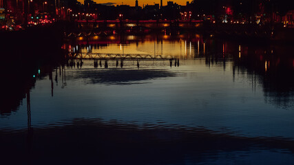 Naklejka premium People walking on a bridge reflected in the river Liffey at sunset, Dublin