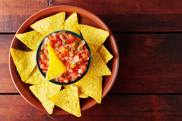 Salsa sauce and nacho chips in a clay bowl. Tortilla chips and salsa dip in bowl on brown boards. Top view. Copy space