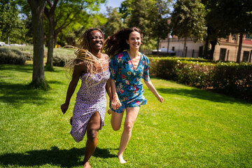 Fototapeta premium Two multiethnic women running holding hands outdoors