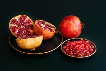 Still life with pomegranates and divided whole grains on black background