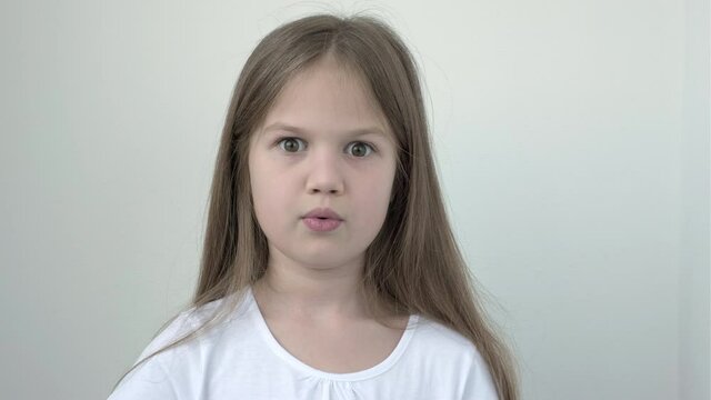 Surprised little girl in white T-short on gray background. Cute child looking at camera happy to receive surprise. Shocked kid face expression. Wow emotion.