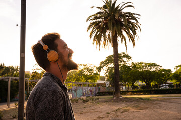 Caucasian man with a beard listening to music with headphones outdoors