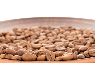 Several fragrant freshly roasted coffee beans on a clay plate, close-up, isolated on white.