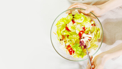 Healthy food. Children 's hands hold glass bowl with salad with herbs, cherry tomatoes, and olive oil with fork on a blue background with copy space. The vegan diet. The concept of simple healthy food