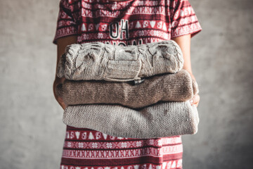 A girl in a Christmas dress holds a stack of sweaters. Warmth, comfort - 479220031