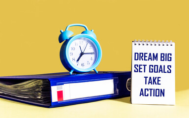Dream Big - Set Goals - Take Action, handwriting in notebook with folder and clock on yellow background