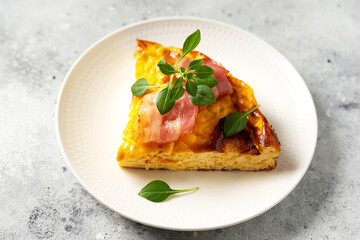 A piece of frittata with pumpkin, bacon and ricotta in a ceramic plate on a light culinary background. Traditional Italian delicious homemade egg dish on the kitchen table closeup	