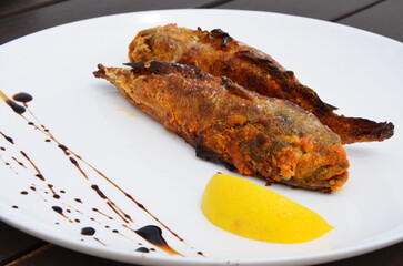 Fried fish and a slice of lemon are on a large white plate.