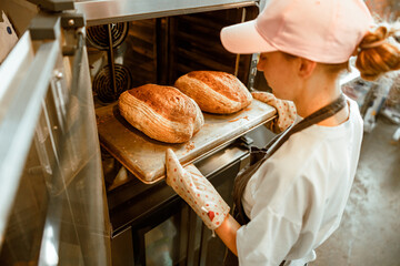 Woman in pink cap takes breads out of oven in craft bakery workshop