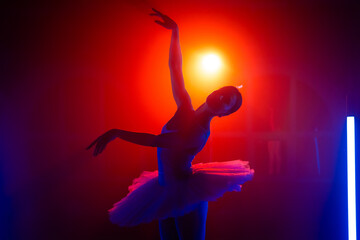 Silhouette of ballerina is practicing elements in studio with neon colorful light. Young woman...
