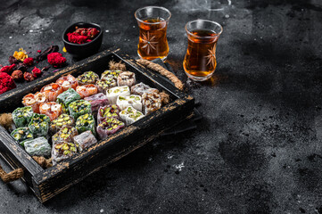 Turkish Delight Lukum, Oriental sweets with nuts and black tea. Black background. Top view. Copy space