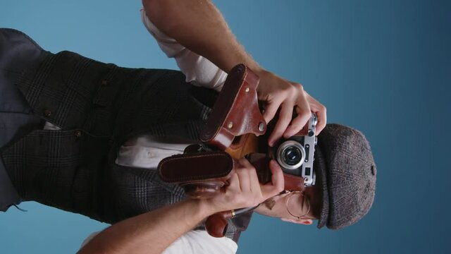 Close up of old fashioned photographer wearing glasses and retro suit with vintage mechanical film camera cocking the shutter gestures with his hands and lines up people in a group photo at studio