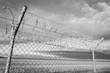 Wide angle view of fence with nato barb wire and razor blades in black and white