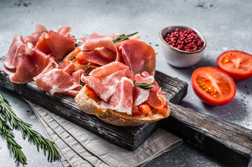 Spanish Tapas - Toast with tomatoes and cured Slices of jamon iberico ham on wooden board. Gray background. Top view - obrazy, fototapety, plakaty