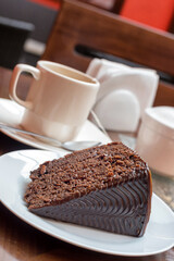 Chocolate cake and cup of tea or coffee in white mug in background