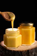 two glass jars with honey and a wooden spoon are depicted on a black background. viscous thick honey on a spoon. the honey holiday was saved.