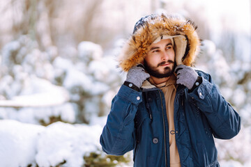 Fototapeta na wymiar Handsome bearded young man standing outdoors fur hood in winter season forest. Season holiday leisure. Nature.